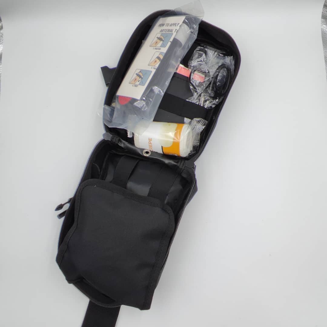 Open first aid pouch with organized medical support supplies including bandages, trauma shears and training accessories